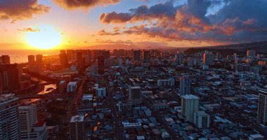 Honolulu, Hawaii, ABD 'nin yoğun kentsel manzarası üzerinde uçuş. Batan güneş gökyüzünü, su manzarasını ve yüksek rıhtımı aydınlatıyor..