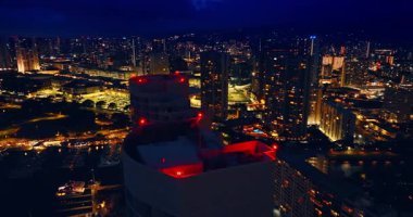 Kırmızı ışıklar açıkken gökdelenlerin tepesine yaklaşıyoruz. Honolulu, Hawaii, ABD 'nin güzel aydınlatılmış gece manzarası. Hava görünümü.