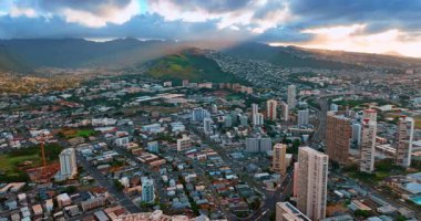 Yoğun şehir manzarası Honolulu, Hawaii, ABD 'den yükseliyor. Işık bulutların arasından yeşil dağlara gider..