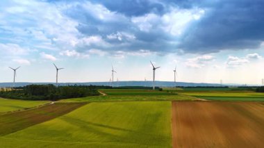 Dramatik bulutlar tarlaların üzerindeki gökyüzünü kaplıyor. Rüzgar türbinleri temiz enerji üretir.