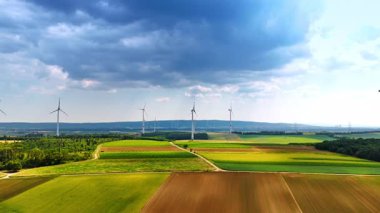 Yağmurlu bulutların altında resimli tarlalar. Rüzgarda dönen bir sürü değirmen var. Hava görünümü.