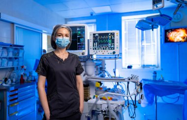 Doktor yüksek teknolojili ameliyathanede. Maske takan ve önlük giyen odaklanmış bir tıp uzmanı gelişmiş monitörlü iyi donanımlı bir ameliyathanede duruyor..