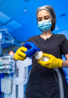 Tıp uzmanı hastane ekipmanlarını kuruyor. Önlüklü bir sağlık görevlisi eldiven ve maske takarak hastane ortamında tıbbi ekipman hazırlar..