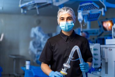 Cerrah ameliyata hazırlanıyor. Genç bir sağlık çalışanı ameliyathanede duruyor. Hasta bakımını sağlamak için gerekli ekipmanlarla ameliyata hazırlanıyor..