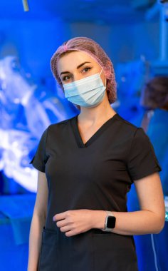 Cerrahi sağlık uzmanı. Maske ve şapka takan bir sağlık personeli ameliyata hazır, parlak bir cerrahi odasında güvenle duruyor..