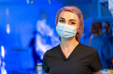 Sağlık sigortası uzmanıyım. Maske takan ve cerrahi başlık takan bir sağlık çalışanı ameliyat sırasında steril bir ortamda güvenle durur..