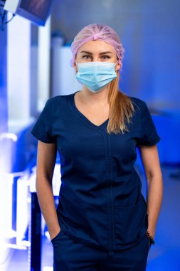 Sağlık hizmetleri çalışanı. Genç bir sağlık çalışanı, maske ve saç filesiyle güvenle tıbbi bir görev için hazır bekliyor..