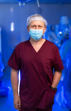 Cerrah anahtar ameliyatı için hazır. Önlüklü bir sağlık uzmanı, bir ameliyat odasında maske takarken ameliyata hazır bir şekilde duruyor..