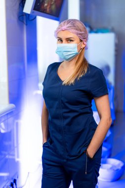 Önlüklü ve maskeli bir doktor. Tıbbi bir tesiste, bir sağlık uzmanı önlük, maske ve bir saç teli takarken rahatça poz verir..