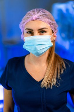 Şapkalı maskeli bir sağlık görevlisi. Bir sağlık görevlisi cerrahi maske ve saç şapkası takıyor ve tıbbi bir ortamda önemli bir göreve hazırlanıyor..