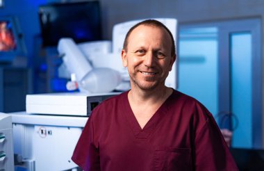 Ameliyathanede gülümseyen doktor. Önlük konusunda kendinden emin bir tıp uzmanı ameliyathanede sıcaklık ve profesyonellik yayar..