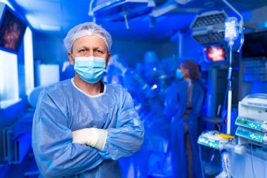 Cerrah ameliyata hazırlanıyor. Ameliyat için ameliyat önlüğü ve maskeli tıp uzmanları modern bir ameliyathanede gelişmiş ekipmanlarla hazır..