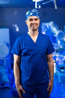Ameliyathanede poz veren bir cerrah. Bir tıp uzmanı, cerrahi önlükler ve iyi donanımlı bir ameliyathane içinde güvenle durur..