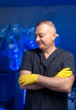 Cerrah ameliyata hazırlanıyor. Sarı eldivenli ve siyah önlüklü bir sağlık çalışanı ameliyata hazır bekliyor..