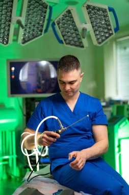 Cerrah ameliyata hazır. Mavi önlüklü bir cerrah teknolojik donanımlı, iyi aydınlatılmış bir ameliyathanede cerrahi bir alet hazırlıyor..