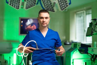 Cerrah ameliyata hazır. Mavi önlüklü bir cerrah ameliyat odasında, elinde cerrahi aletlerle oturup tıbbi bir prosedüre hazırlanıyor..