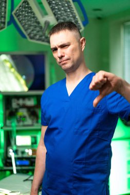 Doktor ofiste bunu onaylamıyor. Mavi önlüklü bir tıp uzmanı klinik ortamda iyi donanımlı bir ofiste onaylanmamış bir jest gösteriyor..