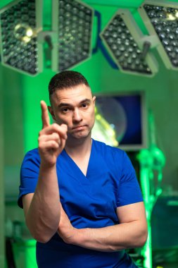 Cerrah ameliyata hazırlanıyor. Mavi önlüklü odaklanmış bir cerrah ameliyata hazır bir ameliyathanede ciddi bir ifadeyle duruyor..