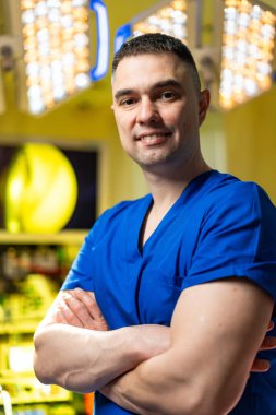 Klinikte kendine güvenen bir profesyonel. Mavi önlüklü kendine güvenen bir sağlık çalışanı kollarını kavuşturup, profesyonellik ve samimiyet saçıyor..