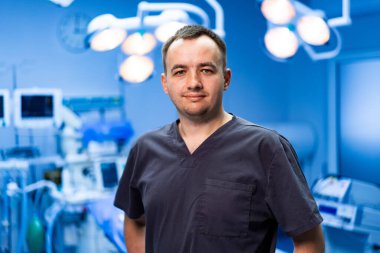 Modern ameliyathanede cerrah. Önlüklü kendine güvenen bir erkek cerrah iyi donanımlı bir ameliyathanede ameliyata hazır..