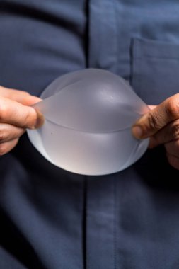 Silikon implantı tutan kişi. Bir insan silikon implantın esnekliğini gösterir. Ellerinin arasındaki şekli ve dokuyu vurgular..