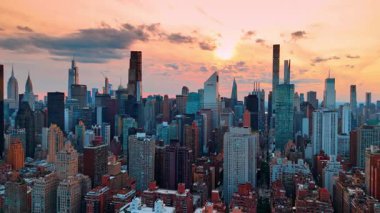 Gün batımında Manhattan 'ın yoğun manzarasının üzerinde uçmak. Gökdelenlerin tepesi Pembe gökyüzünün arkaplanı.