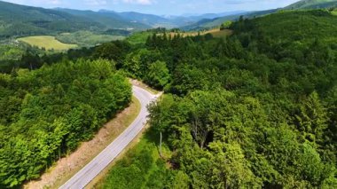 Ağaçlık dağların yeşil yamaçlarında uçmak. Yeşillik ormanların arasından bir otoyol inşa edilir..