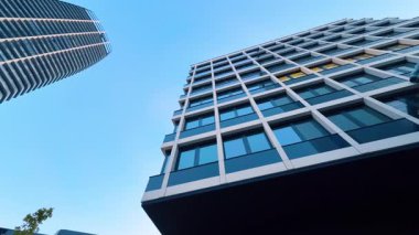 Mavi gökyüzüne karşı modern mimari. İki modern bina mavi gökyüzünün altında parıldıyor, parlak çizgiler ve yansıtıcı cam paneller var..