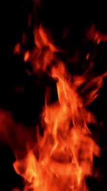 Havada yükselen sıcak kamp ateşi alevleri. Kara arka planda birden fazla kor parçacığı havada uçuşuyor. Dikey video