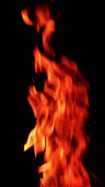 Karanlığın içinde yanan ateşin uzun ve ince alevi izole. Havada minik parıltılar yükseliyor. Dikey video