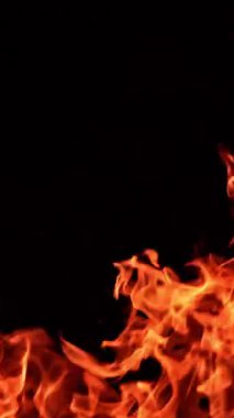 Karanlıkta dans eden öfkeli alevler. Turuncu alevler yükselip yükseliyor. Kapatın. Dikey video