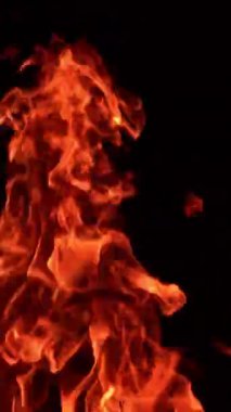 Karanlıkta hareket eden alevin kırmızı dilleri. Sıcak alevler izole edilmiş, kıvılcımlar uçuşuyor. Kapatın. Dikey video