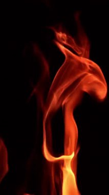 Gecenin içinde ateş dansı yapmak. Siyah arka planda alevlerin büyüleyici dilleri. Kapatın. Dikey video