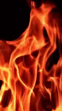 Büyük kamp ateşinde alevler var. Yangından çıkan yanmış ahşap. Kapatın. Siyah zemin. Dikey video