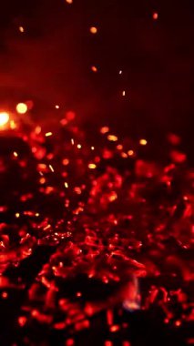 Kızgın kırmızı közler çubuk tarafından hareket ettirilir. Parlak parıltılar havada uçuşuyor. Siyah zemin. Dikey video