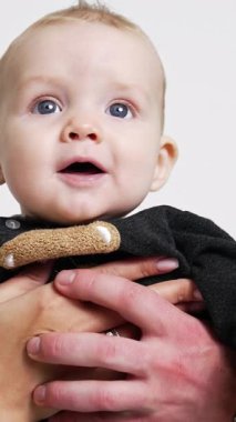 Ebeveynler sevgili küçük oğullarını iki taraftan tutarlar. Sevgi dolu anne ve baba, çocuklarını başından öperler. Beyaz zemin. Dikey video