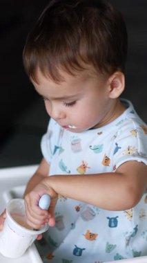 Plastik bardaktan kaşığı yoğurtla dolduran tatlı bir çocuk. Süt ürünleri ile lezzetli sağlıklı atıştırmalıklar. Üst Manzara. Dikey video