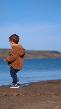 Rıhtımda taşlarla oynayan mutlu çocuk. Sonbahar yaz gününde doğada heyecan verici zaman harcamak. Dikey video