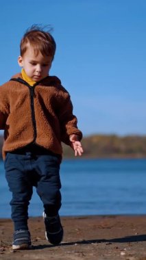 Sevimli erkek çocuk sahilde el çırpıyor. Yürüyen bir taş alır, suya koşar ve taşı fırlatır. Dikey video