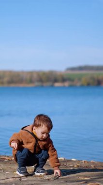 Küçük Kafkas çocuk nehir kıyısında. Küçük oğlan sopayı suya sokuyor. Doğada güneşli bir sonbahar günü. Dikey video
