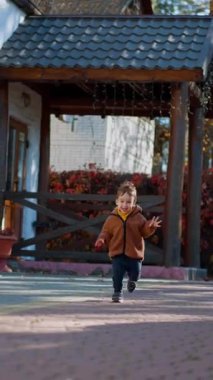 Sevimli gülümseyen çocuk kameraya doğru koşuyor. Mutlu erkek bebek sonbaharda açık havada vakit geçiriyor. Dikey video