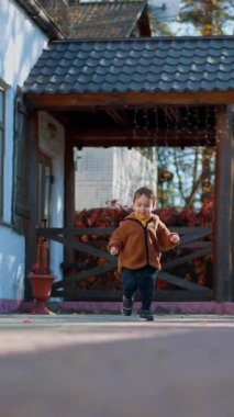 Sonbaharda avluda koşan neşeli beyaz çocuk. Güneşli bir günde enerjik ve aktif bir yürüyüş. Dikey video