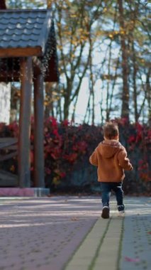 Sonbaharda dışarıda koşan enerjik bir çocuğun arka görüntüsü. Küçük oğlan evin verandasına koşuyor. Dikey video