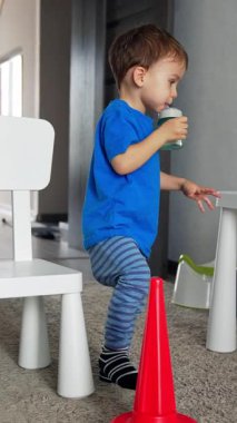 Şişeden su içen tatlı çocuk. Küçük çocuk beyaz sandalyeye dikkatlice oturur. Dikey video