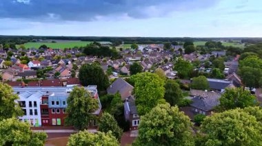 Yeşil ağaçların üzerinden uçarak benzer konutlara yaklaşıyorlar. Hollanda 'nın güzel Vierlingsbeek kasabası bulutlu bir günde.