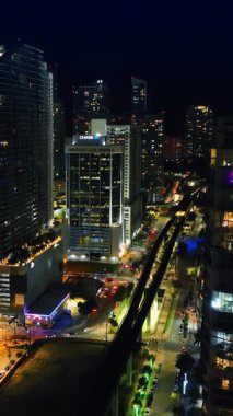 Gece şehrinin üstündeki gökdelenler arasında uçmak. Akşamları Miami, Florida 'nın aydınlık sokaklarının en iyi manzarası. Dikey video