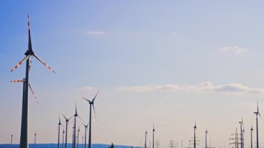 Türbinler temiz enerji üretir. Berrak mavi gökyüzünün altındaki yemyeşil alanlar üzerinde geniş rüzgar türbinleri kulesi yenilenebilir enerji üretimi sergiliyor.