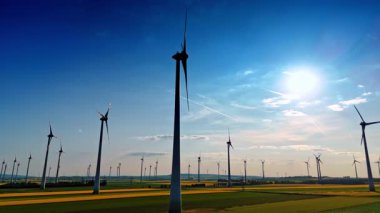 Günbatımı rüzgar türbinleri üretiyor. Rüzgâr türbinleri, güneş batarken manzaralı bir arazide dimdik ayakta duruyor ve yenilenebilir enerjiyi iş başında gösteriyor..