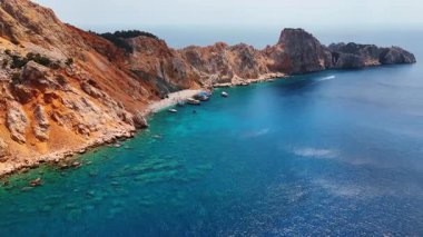 Engebeli uçurumların kıyı manzarası. Canlı turkuaz sular, berrak gökyüzünün altında engebeli bir kıyı şeridi boyunca uzanan engebeli uçurumlarla buluşur ve sakin bir manzarayı gözler önüne serer..