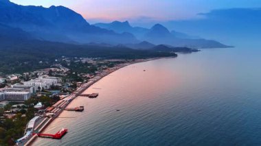 Gün batımında sakin bir körfezin üzerinde kıyı manzarası. Alacakaranlık sakin bir körfeze yerleşir, dağları, kıyı şeridini ve yumuşak renkleri yansıtan huzurlu suları gözler önüne serer..